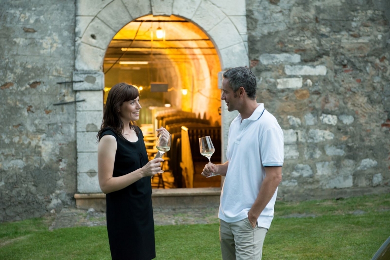 Eine Frau und ein Mann genießen ein Glas Wein vor dem beleuchteten Eingang des Bischöflichen Weinkellers