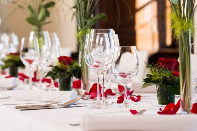 Drei Weingläser strahlen von einer wunderschön dekorierten Festtafel. Rote Blüten und Gräser zieren die Tische