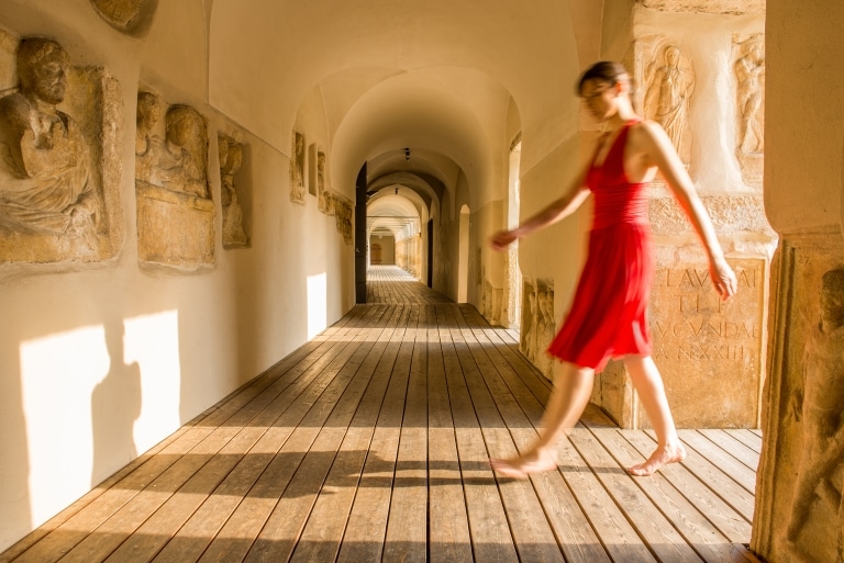 A lady dressed in a red dress walks through the arcades at Seggau Castle.